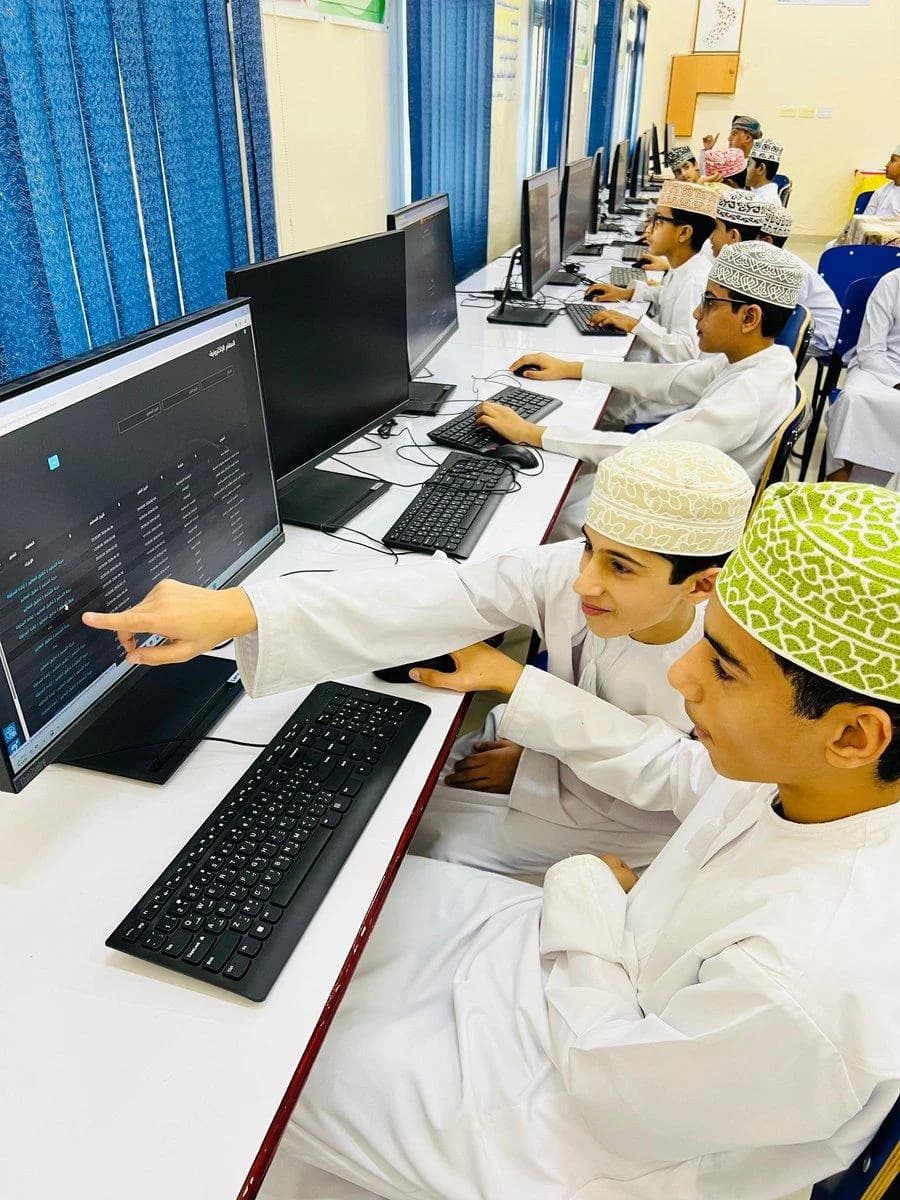 طالبان يشيران إلى شاشة حاسوب تعرض نظامًا إلكترونيًا بالعربية في مختبر الحاسوب