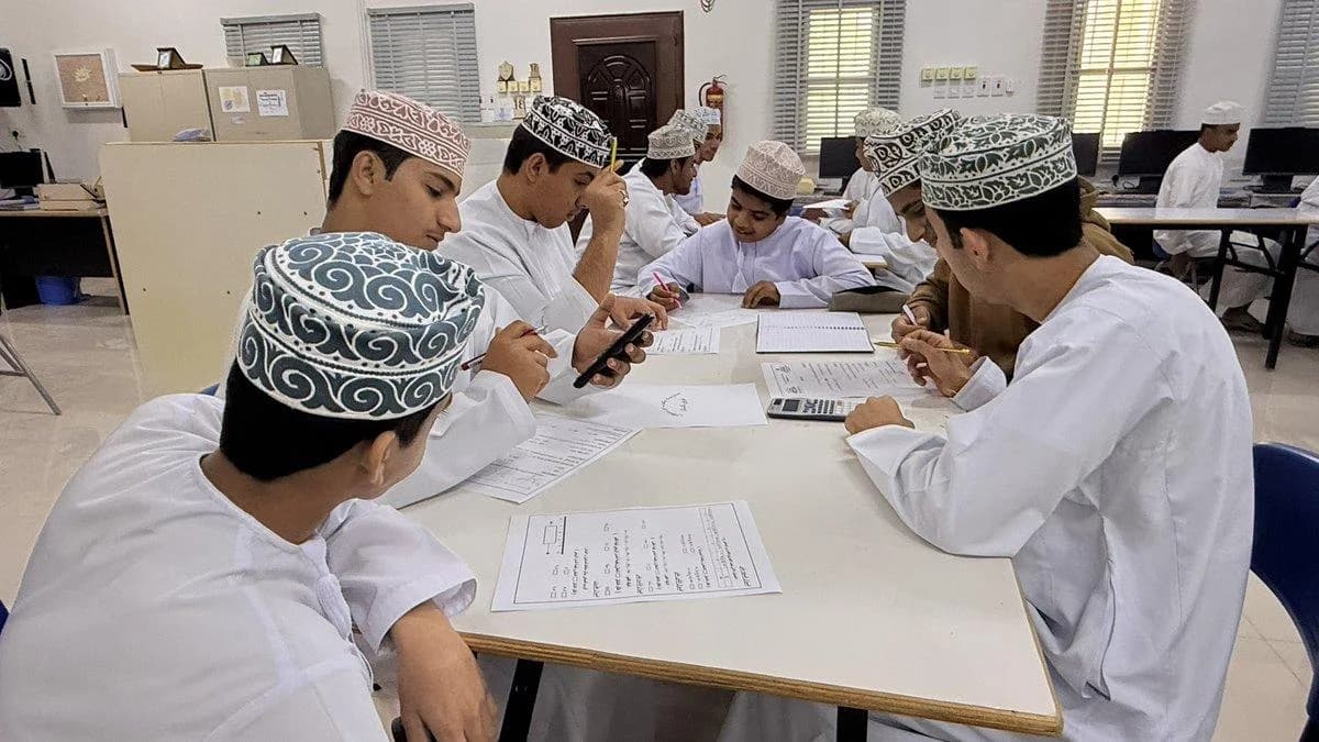 ستة طلاب حول طاولة يملؤون استمارات ورقية بأقلامهم، ومعهم آلة حاسبة